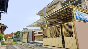 Edificio residencial con entrada protegida por un portón, balcón y un letrero que anuncia un servicio de alquiler de viviendas.