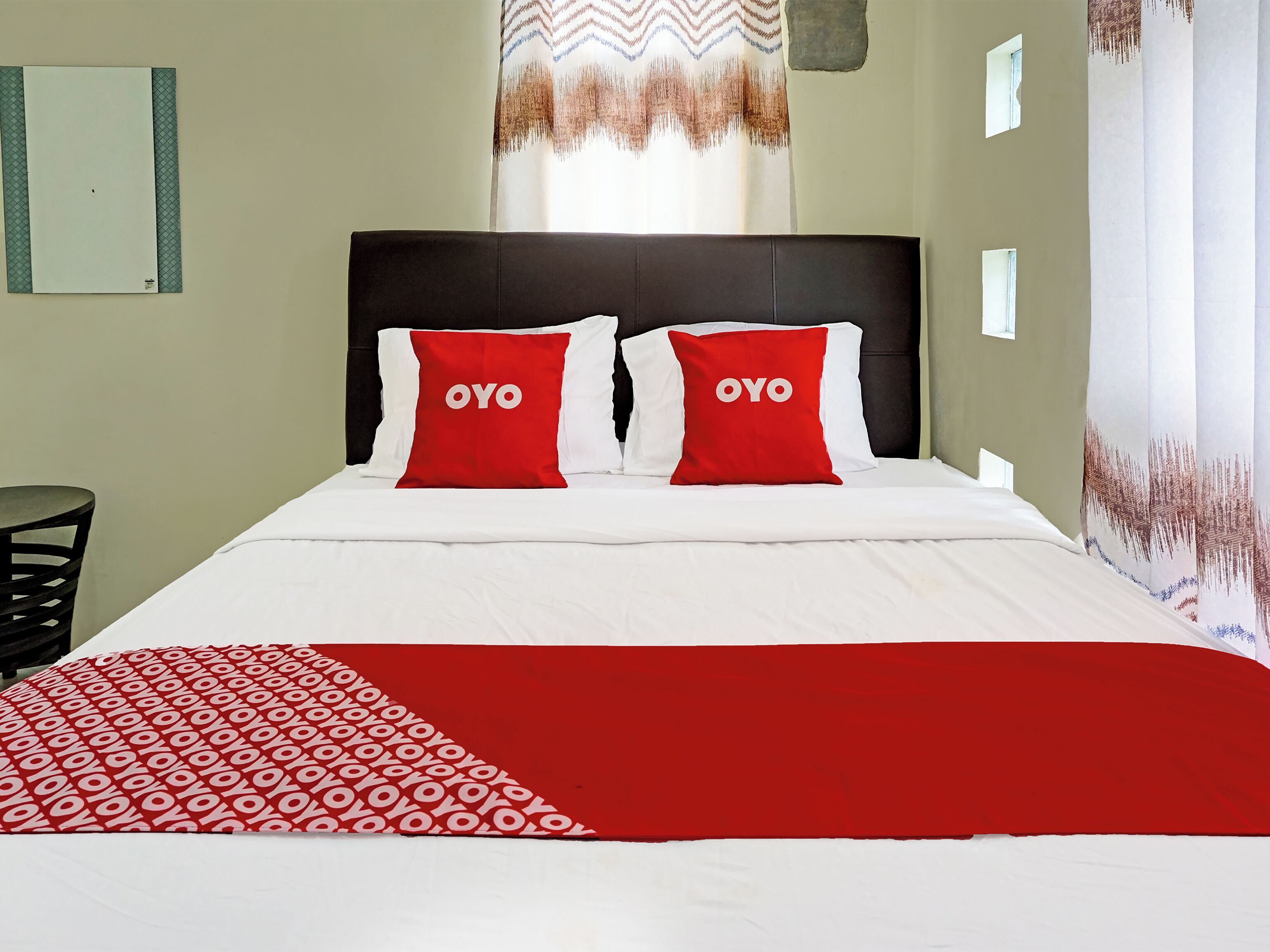 Ein Hotelzimmer mit einem Bett, zwei rote Kissen mit dem Schriftzug 'OYO', einer weißen Bettdecke und einer rot-weißen Tagesdecke.
