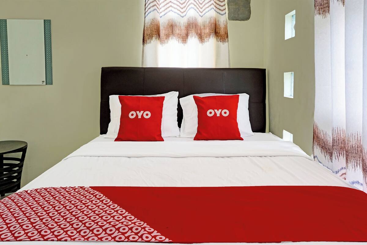 Ein Hotelzimmer mit einem Bett, zwei rote Kissen mit dem Schriftzug 'OYO', einer weißen Bettdecke und einer rot-weißen Tagesdecke.