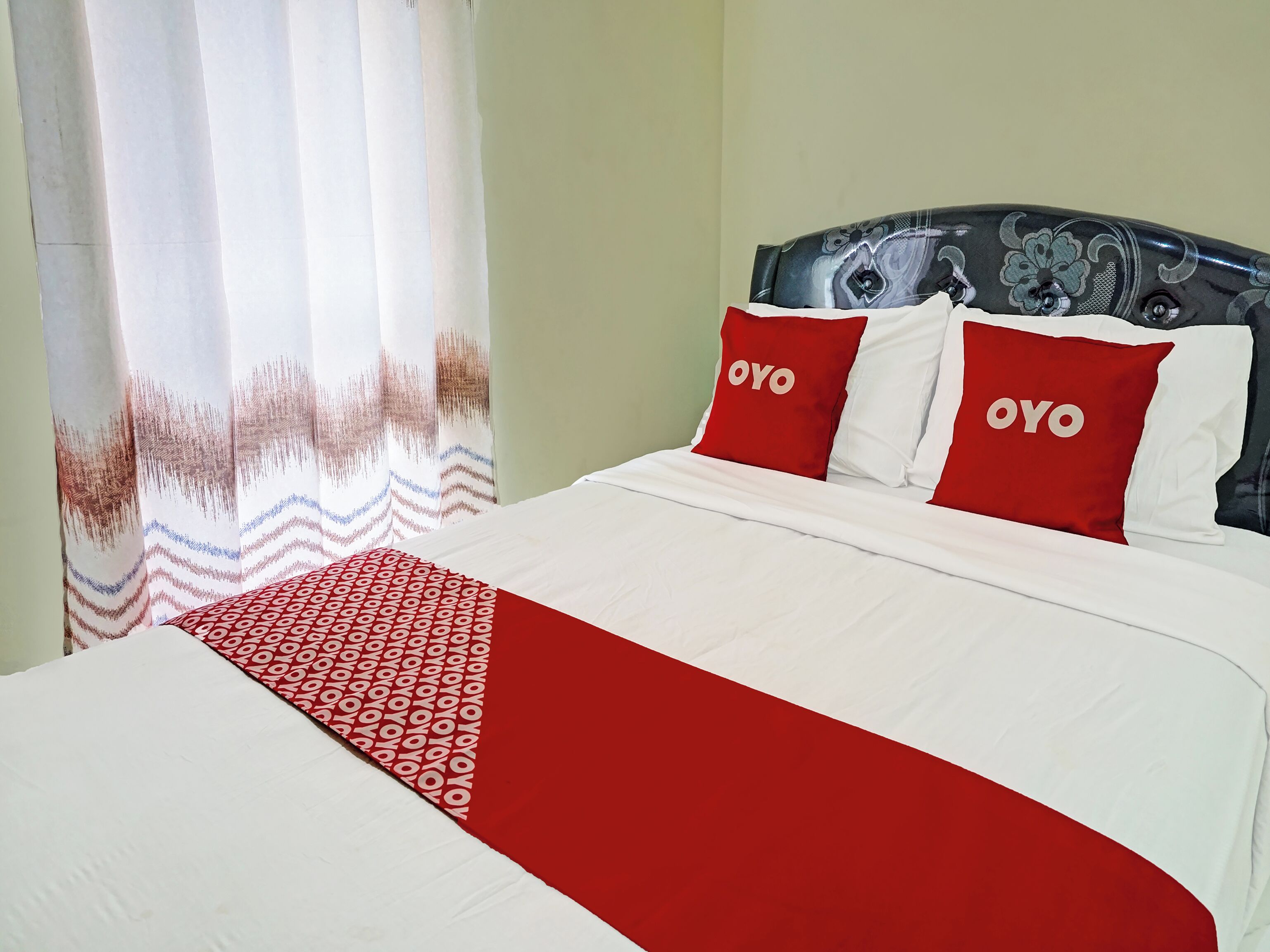 Ein Bett mit weißer und roter Bettwäsche, zwei Kissen mit dem Schriftzug 'OYO' und einer gemusterten Decke.
