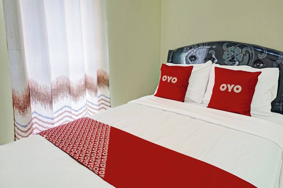 Ein Bett mit weißer und roter Bettwäsche, zwei Kissen mit dem Schriftzug 'OYO' und einer gemusterten Decke.