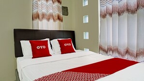 Una cama bien hecha con una colcha blanca y roja, dos almohadas rojas con el texto 'OYO' y una manta roja con un estampado.