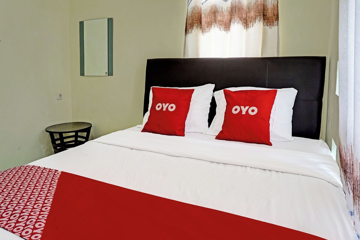 Een hotelkamer met een bed, twee kussens met 'OYO'-branding, een nachtkastje en een spiegel aan de muur.