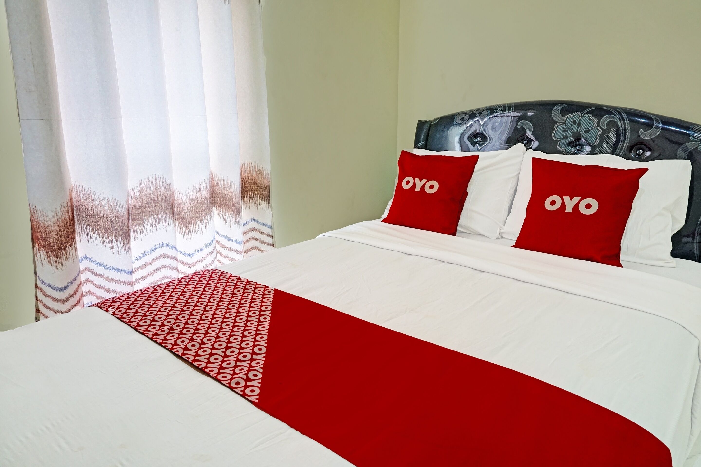 Una cama bien hecha con una colcha roja y blanca, dos almohadas con la palabra "OYO" y un plaid estampado.