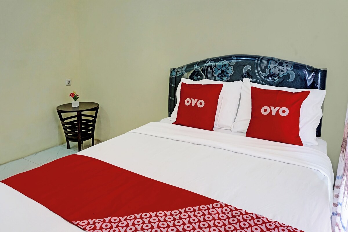 Een bed met twee OYO kussens, een rood-wit geborreld dekbed en een klein tafeltje met een bloempot.
