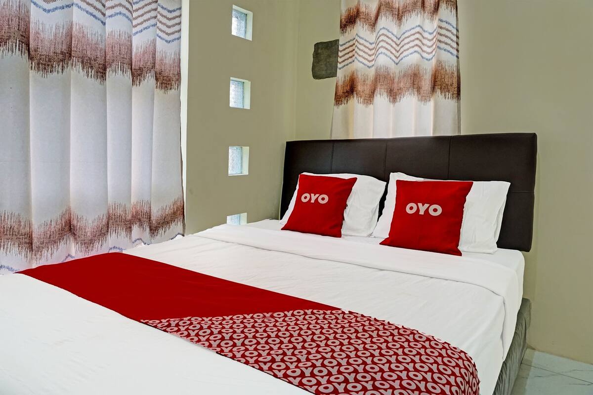 Ein ordentlich bezogenes Bett mit einer rot-weißen Bettdecke und zwei roten Kissen mit dem Schriftzug "OYO".