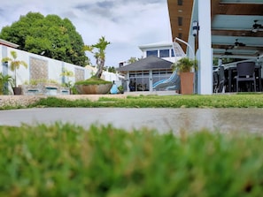 Un bâtiment moderne doté d’un espace extérieur aménagé avec une zone de sièges couverte, d’un grand bac à fleurs et d’un arbre en arrière-plan.