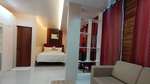 A bedroom with a bed, a wooden floor, a red curtain, and a beige sofa.