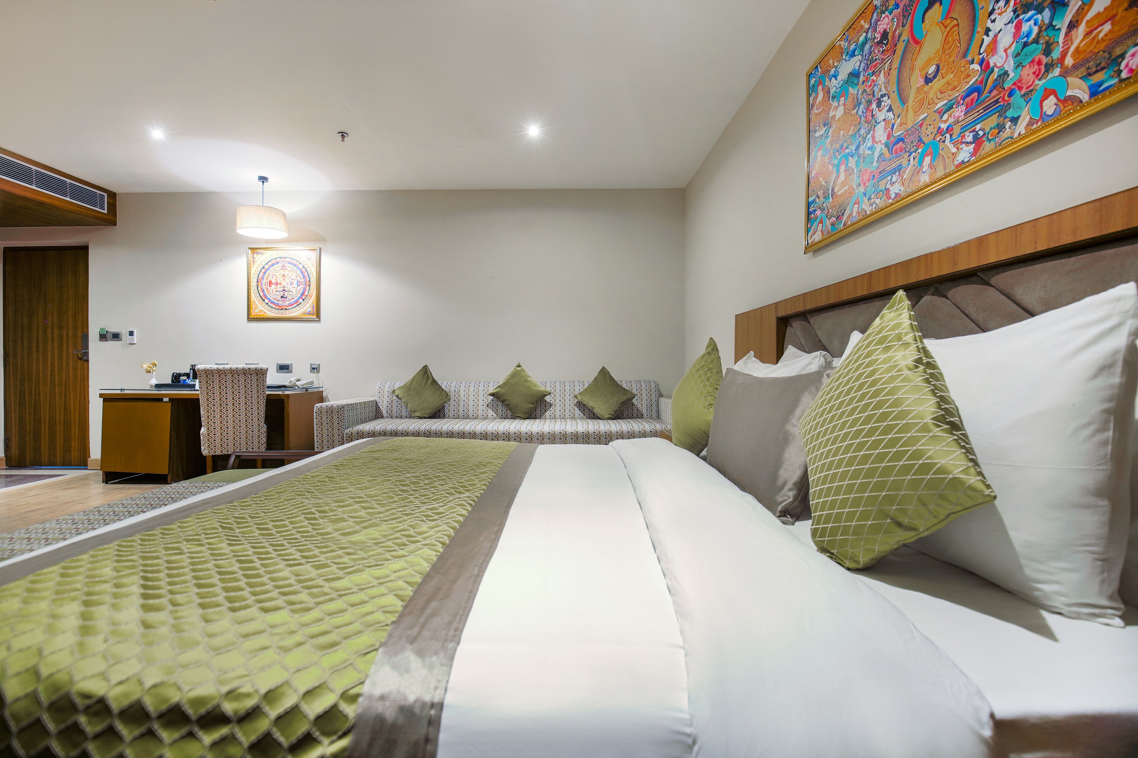 A hotel room with a large bed, a desk, a chair, and a sofa with pillows.