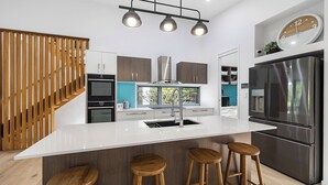 A modern kitchen with a central island, stainless steel appliances, and wooden accents. - Stunning House in peaceful coastal setting (Coolum Beach)