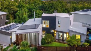 A modern two-story house with solar panels, a well-maintained garden, and a view of the surrounding landscape. - Stunning House in peaceful coastal setting (Coolum Beach)