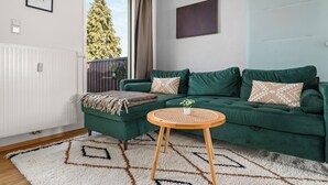 A green sofa with patterned cushions, a small round table with a plant, and a white radiator. - Tucan - Rooftop Terrace With View, Bbq, Ps4+streaming (Marburg)