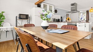 A modern kitchen with white cabinets, a wooden dining table, and a vase with flowers. - Tucan - Rooftop Terrace With View, Bbq, Ps4+streaming (Marburg)