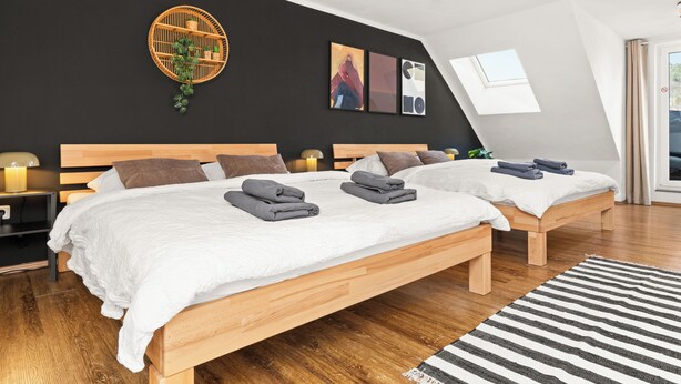 A modern bedroom with two beds, a black accent wall, a wooden headboard, a small window, and a black and white striped rug. - Tucan - Rooftop Terrace With View, Bbq, Ps4+streaming (Marburg)