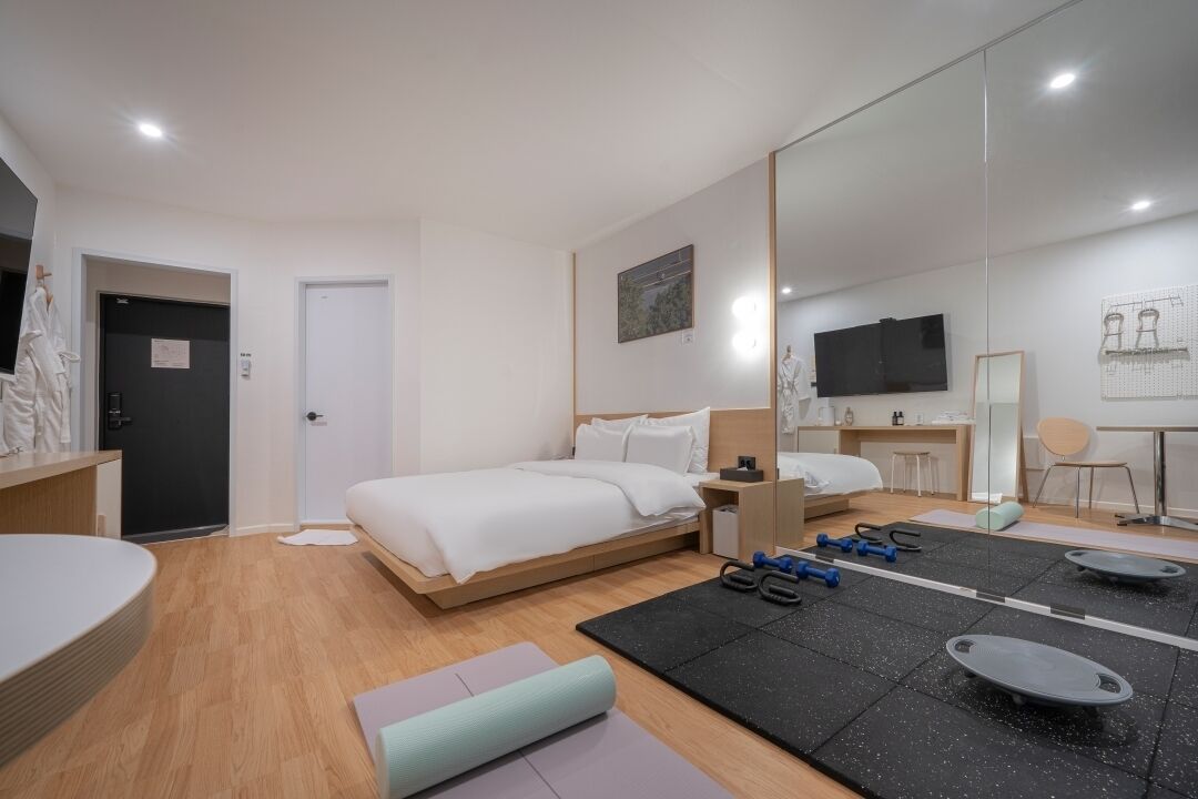Ein modernes Hotelzimmer mit einem Bett, Trainingsgeräten, einem Schreibtisch und einem Fernseher.