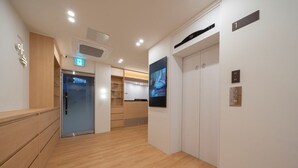 Una hall moderna di un hotel con pavimento in legno, una reception, un orologio digitale e un ascensore.