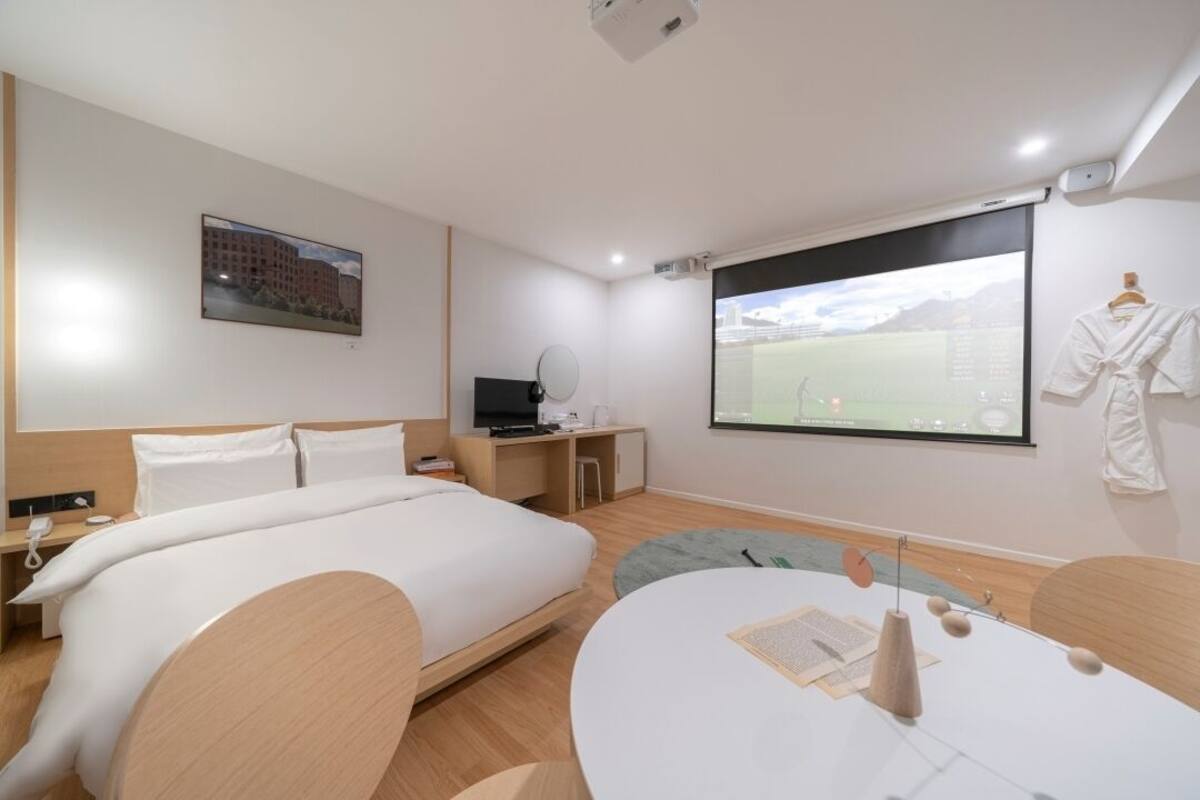 Ein Hotelzimmer mit Bett, Schreibtisch, Fernseher, Projektionsleinwand und einem Kleiderhaken für Bademäntel.