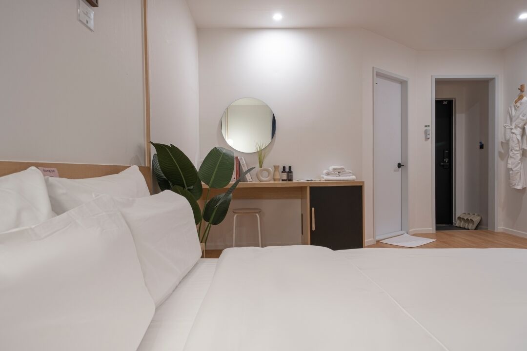 A hotel room with a large bed, a desk with a mirror, a small cabinet, and a plant.