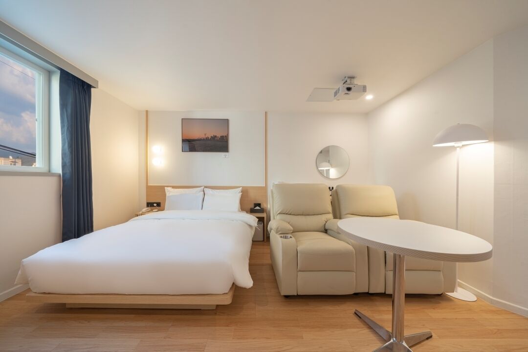 Una habitación de hotel con una cama, un sofá, una mesita, una lámpara y un cuadro en la pared.