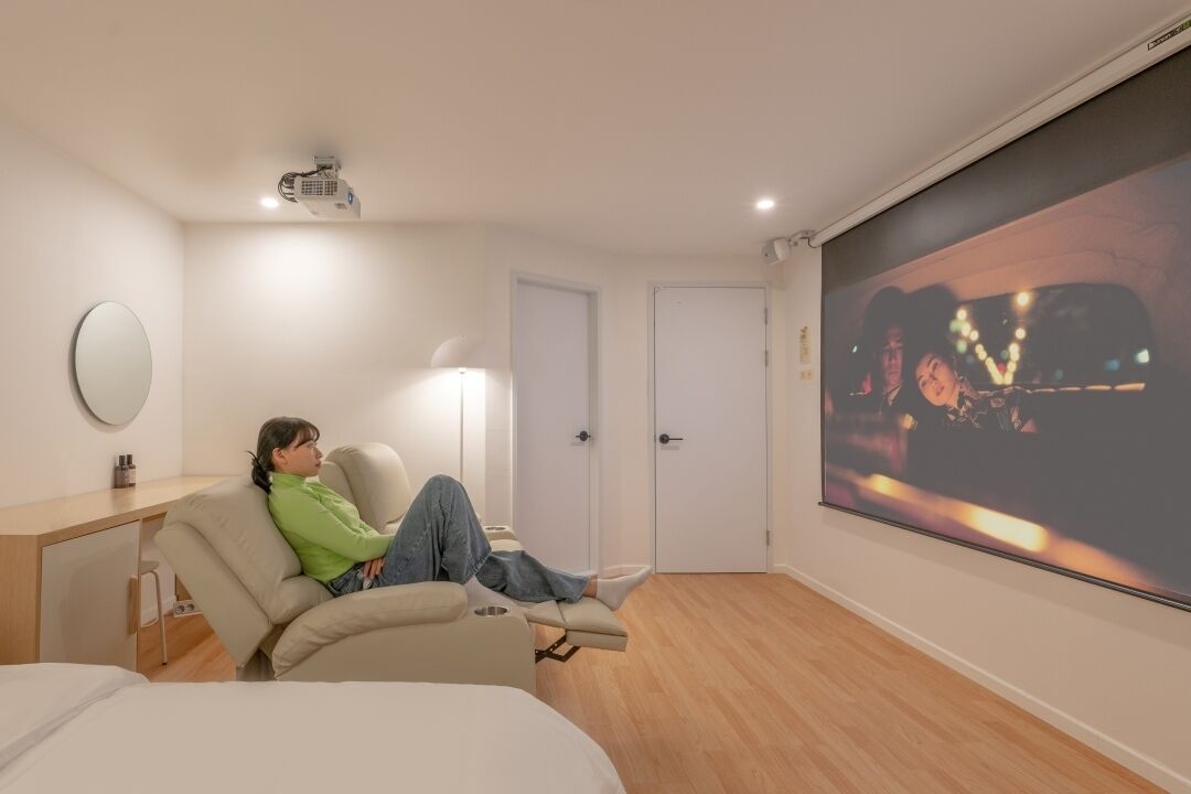 A room with a bed, a reclining chair, a large screen, and a door.