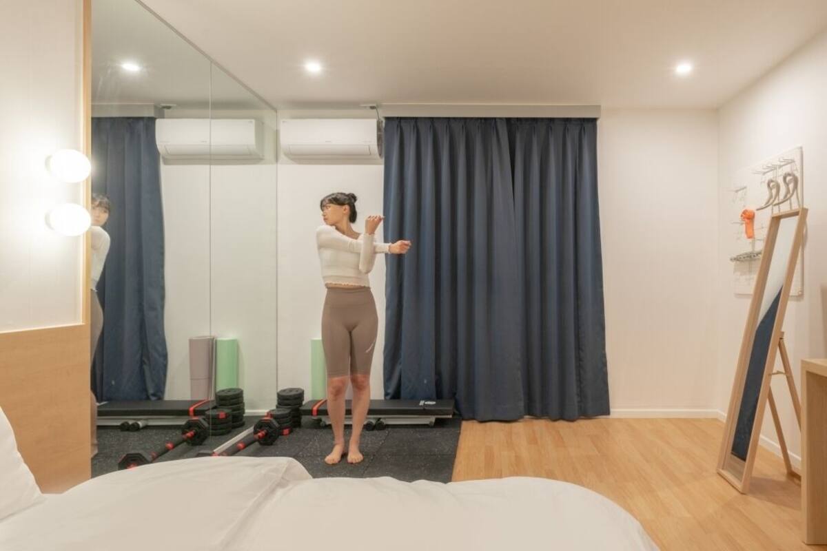 Ein Zimmer mit Bett, Spiegel, Trainingsbereich inklusive Gewichten und einem Bild an der Wand.
