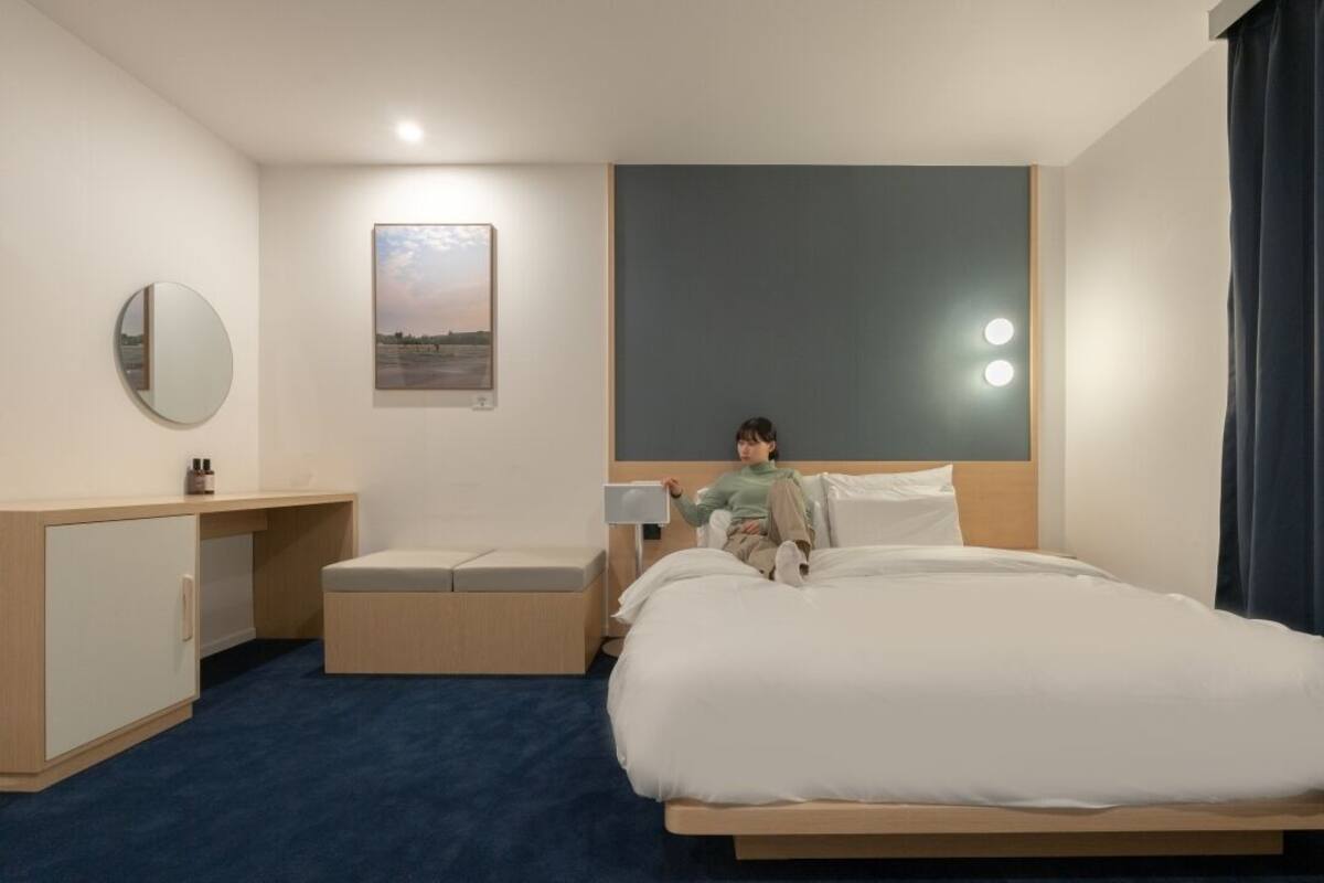 Ein Hotelzimmer mit Bett, Nachttisch, Spiegel, einem an der Wand hängenden Bild und einem Beistelltisch mit Lampe.