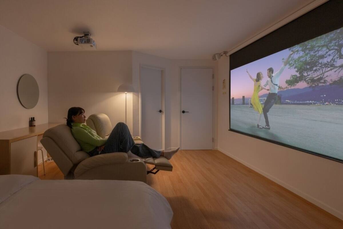 Ein Zimmer mit einem großen Bildschirm, der ein tanzendes Paar zeigt, einem Sofa, einer Lampe und einer Tür.
