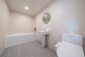 Un baño moderno con bañera, lavamanos, inodoro y un espejo redondo en la pared.
