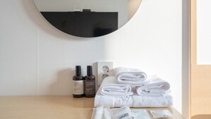 Camera d'hotel con uno specchio rotondo, un tavolino da toeletta in legno, asciugamani bianchi ordinatamente piegati e articoli da toilette.