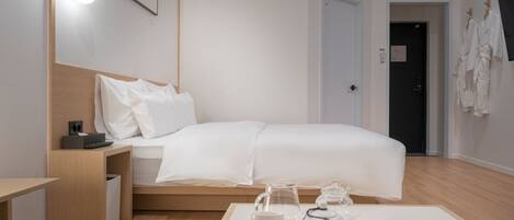 A modern hotel room with a neatly made bed, bedside table with a lamp, and a tray with tea and books.