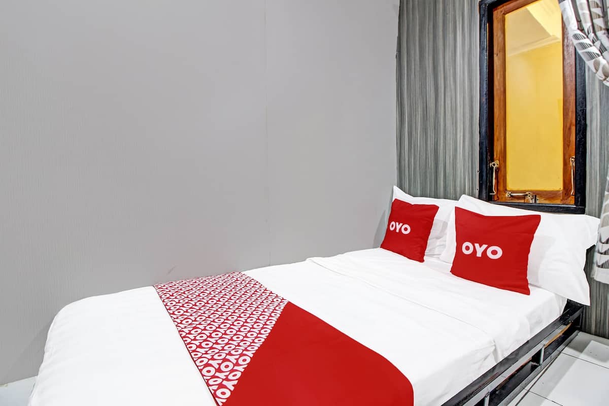 Ein Hotelzimmer mit einem Bett, zwei rote Kissen mit dem "OYO"-Branding, einer weiß-roten Bettdecke und einem Fenster mit Vorhängen.