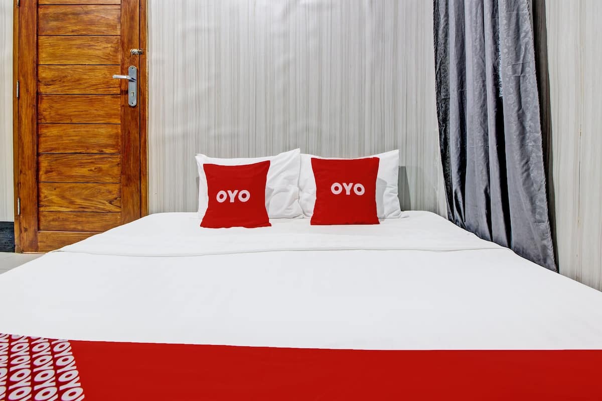 Ein Bett mit weißer Bettwäsche und zwei roten Kissen mit dem Aufdruck "OYO", eine Holztür und ein Streifenmuster-Vorhang.