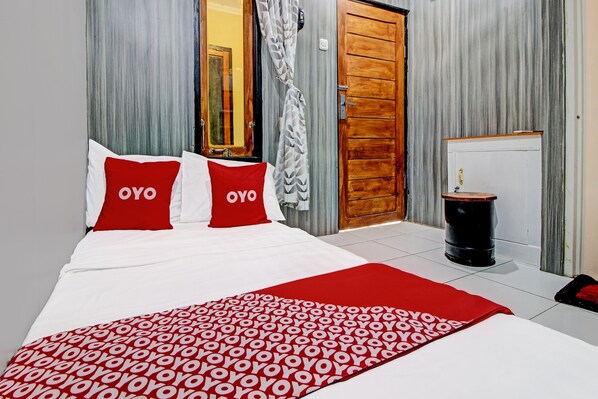 Una habitación de hotel con una cama, una manta estampada en rojo y blanco, y una puerta de madera.