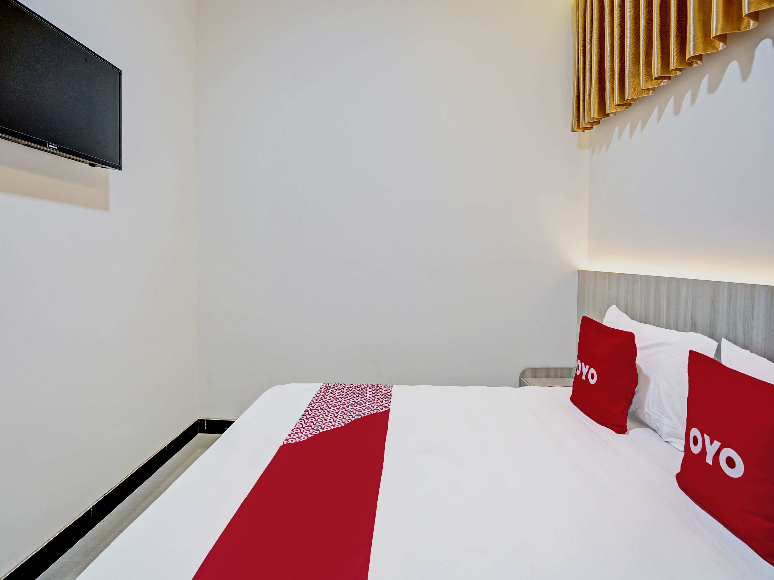 A hotel room with a bed, a flat-screen TV mounted on the wall, and a decorative wall panel.