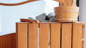 Una sauna de madera con un banco de madera, un balde de madera y una cuenca llena de piedras.