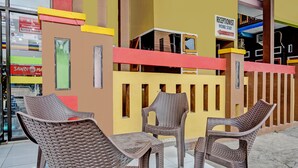 A reception area with a reception desk, a receptionist sign, and a sign indicating a home stay option. There are wicker chairs and a table in front of the desk.