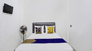 A small, white room with a bed, a wall-mounted TV, and a standing fan.
