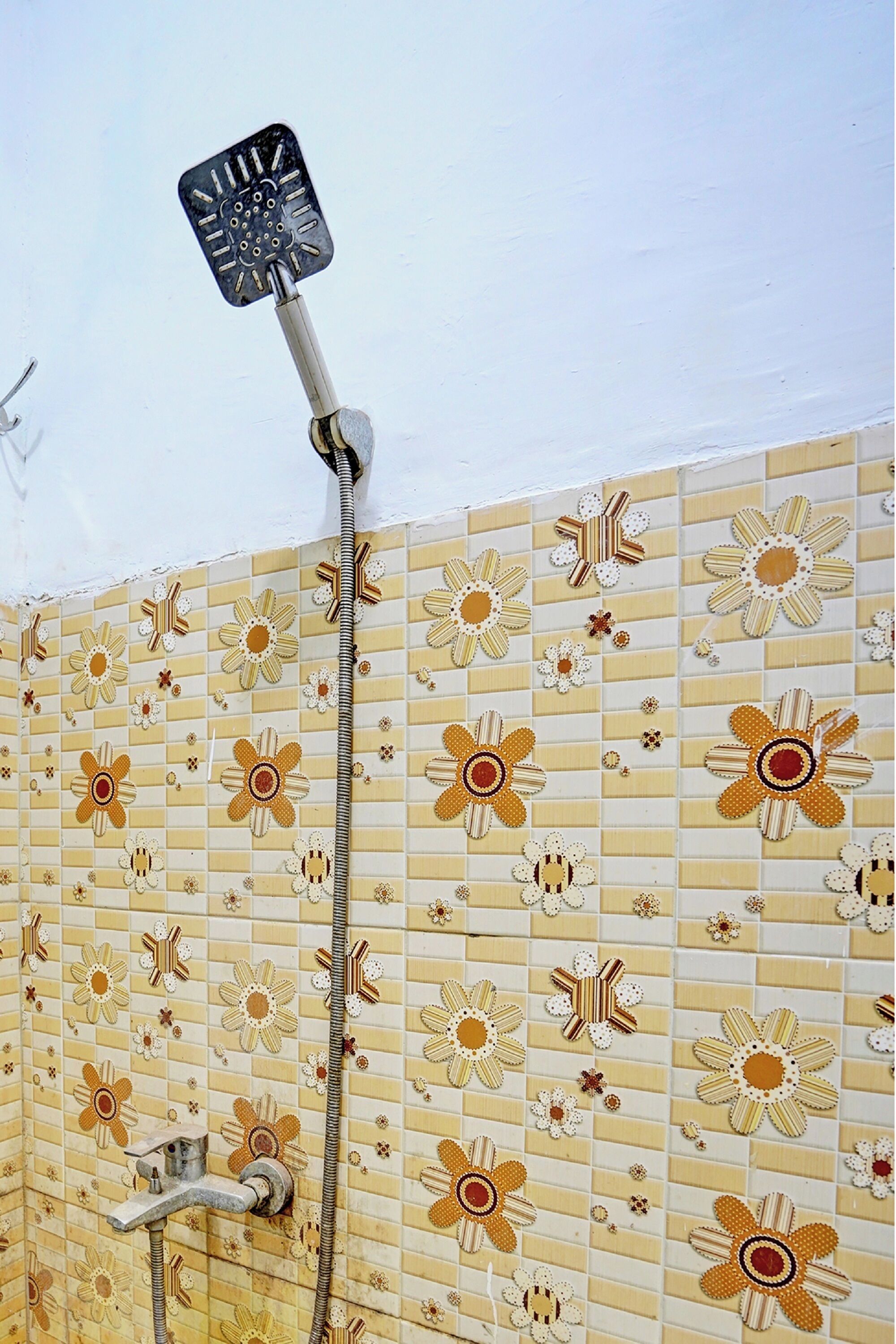 Une douche avec des carreaux à motifs floraux et un pommeau de douche amovible.