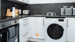 A modern kitchen with white cabinets, a black washing machine, a built-in oven, and a microwave.