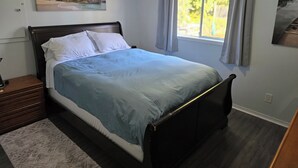A bedroom with a bed, a nightstand, a window with curtains, and a painting on the wall.