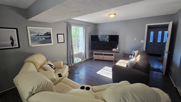 A modern living room with a large flat-screen TV, a beige sofa, a brown armchair, and a glass coffee table.