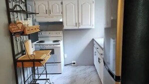 A compact kitchen with white cabinets, a black refrigerator, and a small dining table with a chair.