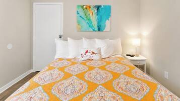 Une chambre à coucher avec un lit, des oreillers, une table de chevet, une lampe et un tableau au mur.
