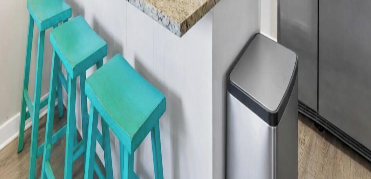 Une cuisine équipée d’un réfrigérateur en acier inoxydable, d’un plan de travail blanc et de trois tabourets turquoise.
