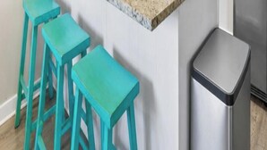 A kitchen with a stainless steel refrigerator, a white countertop, and three turquoise stools.