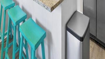Une cuisine équipée d’un réfrigérateur en acier inoxydable, d’un plan de travail blanc et de trois tabourets turquoise.
