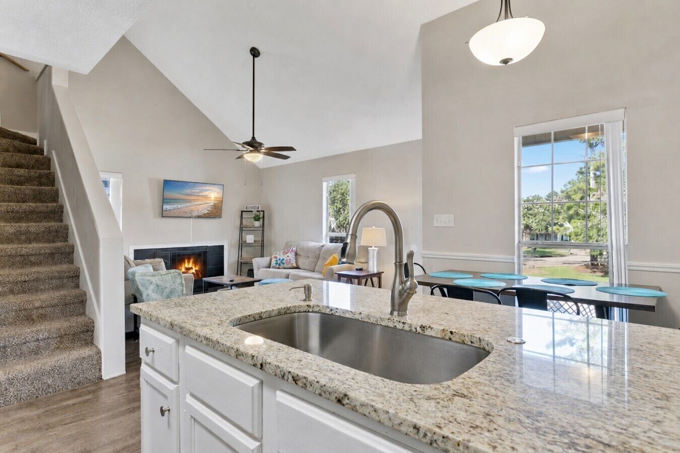 A kitchen with a granite countertop, stainless steel sink, and a dining area with a table and chairs.