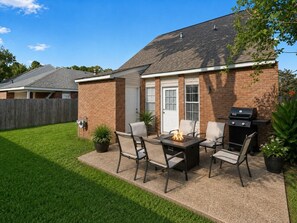 A backyard with a patio table and chairs, a barbecue grill, and a brick house.