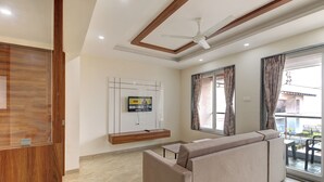 A modern living room with a sofa, a mounted TV, and a ceiling fan. -  Ovi Resort and Spa (Mawal)