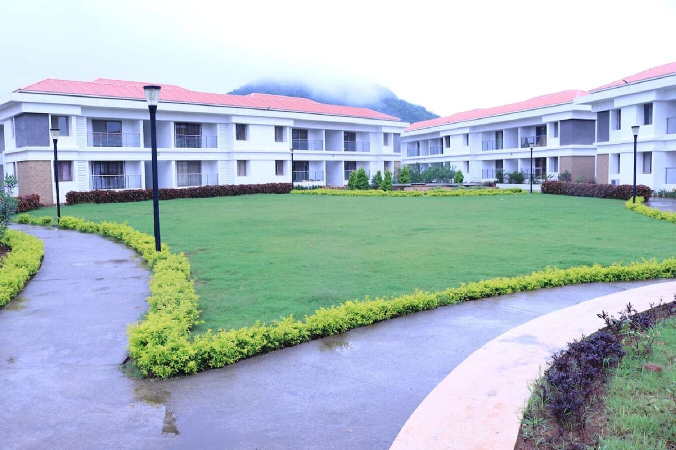 A multi-story hotel with a red roof, a central lawn, and a paved walkway.